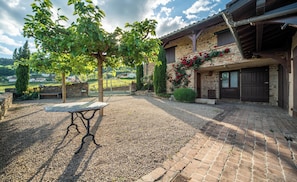 A courtyard with a gravel path, a bench, and a building with a stone facade and a wooden door.