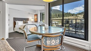 A modern hotel room with a glass dining table, comfortable seating, a large window with a mountain view, and a separate bedroom area. - BEST Location! Stunning Mountain Views, Ski-in/Ski-out, Base of both lifts!⛷🚠 (Whistler)