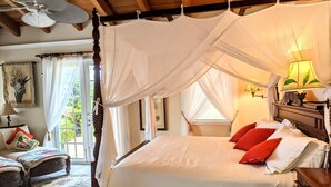 Een slaapkamer met een hemelbed, een houten hoofdbord, een nachtkastje met lamp, en uitzicht op de natuur door een raam.