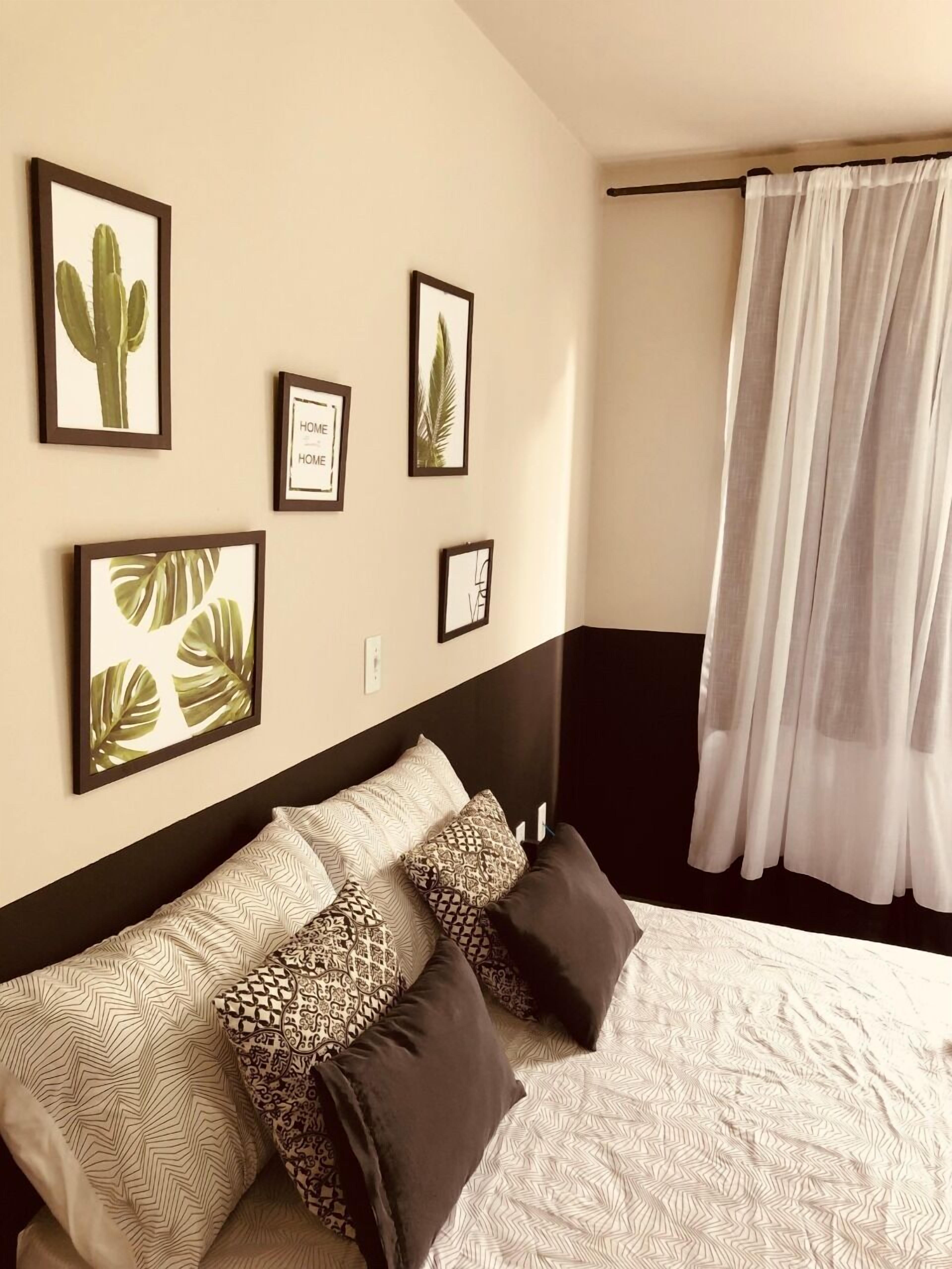 A bedroom with a bed, pillows, a headboard, and framed pictures on the wall.