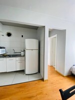 Uma cozinha compacta com armários brancos, pia, micro-ondas e geladeira.