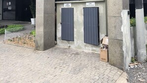 La entrada al edificio Abdon, con un amplio frente de vidrio y dos puertas grises identificadas como "LIXO COMUM" y "LIXO RECICLÁVEL".