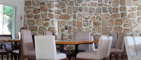 A restaurant with stone walls, wooden tables, and cushioned chairs.