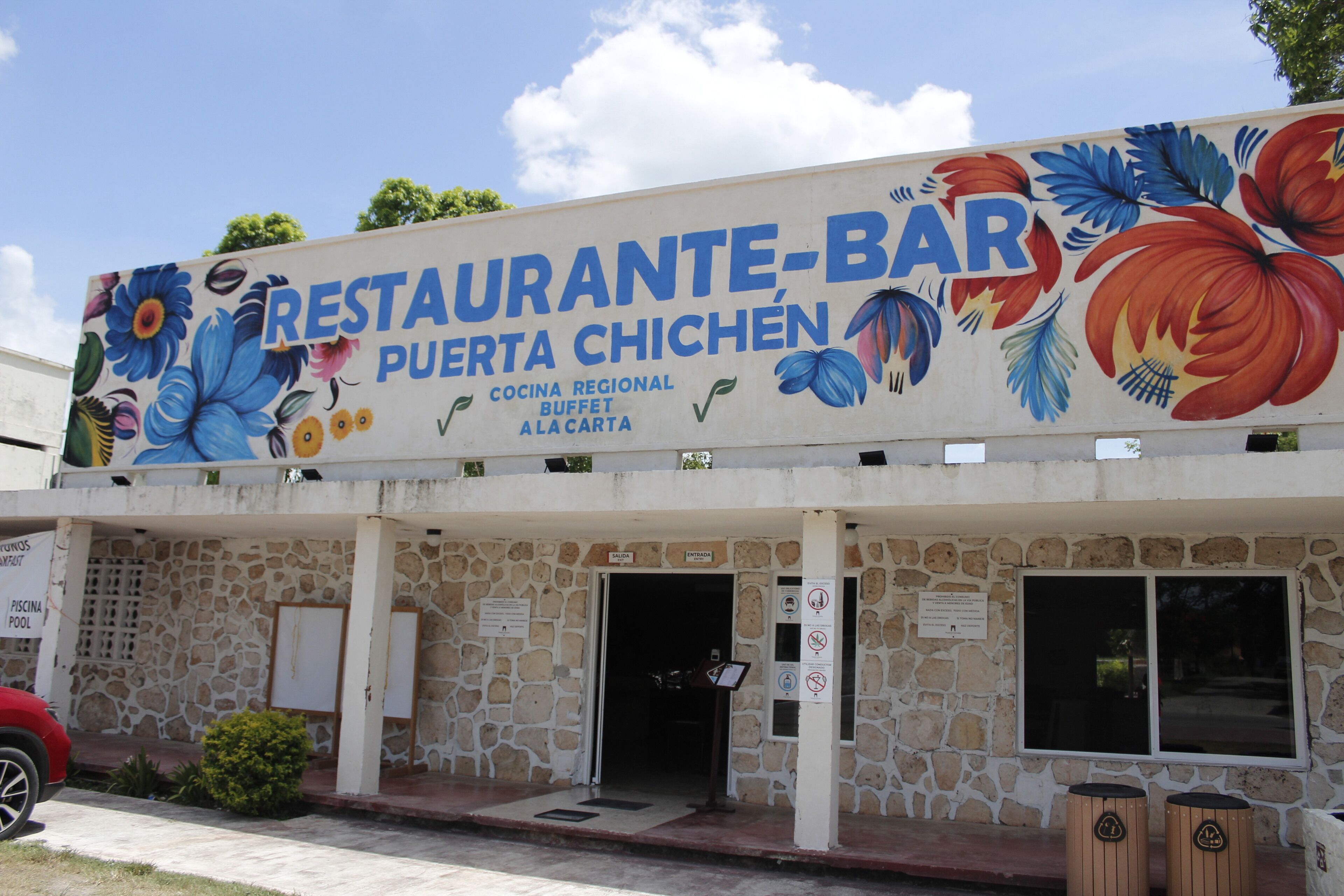 Un restaurante con un mural colorido, fachada de piedra y un letrero que indica que es un bufé.
