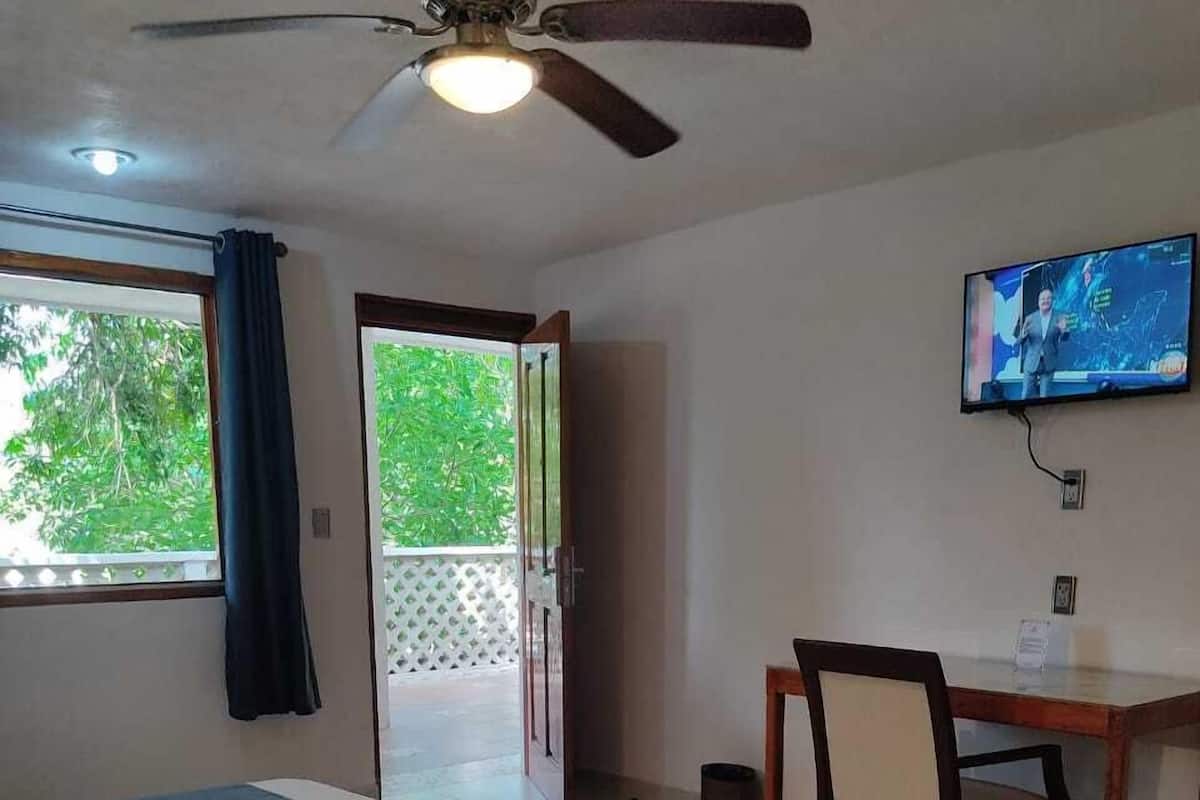 Ein Hotelzimmer mit Bett, Schreibtisch, Stuhl, Fernseher und Deckenventilator.