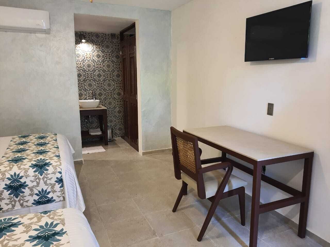 Una habitación con cama, escritorio, silla, televisor y baño con lavamanos y papel tapiz estampado.