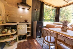 Interior acogedor de una cabaña con detalles de madera, una estufa, un refrigerador y una ventana con vistas a árboles.