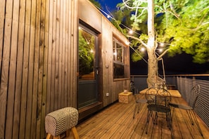 A wooden deck with a table and chairs, a small bench, and a tree with string lights.