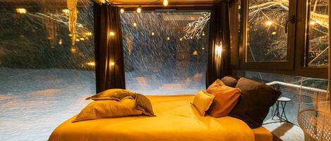 Un lit donnant sur un paysage enneigé, visible à travers une grande fenêtre.
