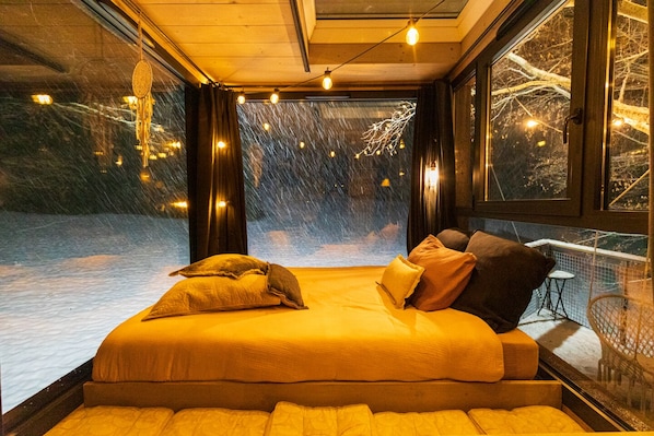 A bed with a view of a snowy landscape through a large window.