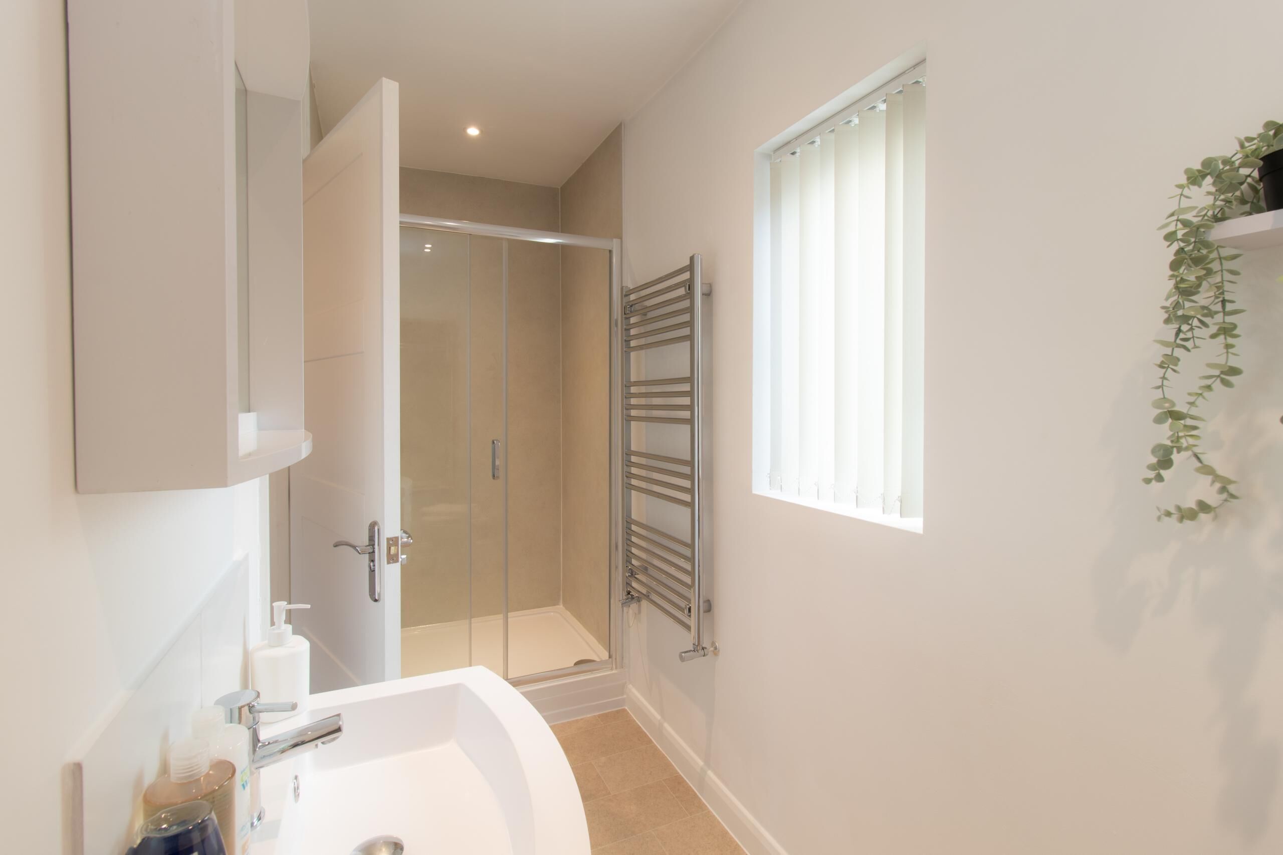 A modern bathroom with a shower, a large mirror, and a window with blinds.