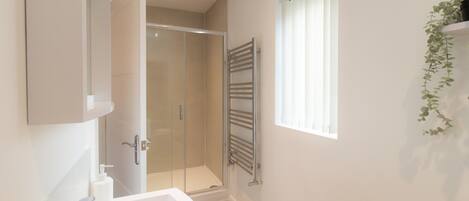 A modern bathroom with a shower, a large mirror, and a window with blinds.
