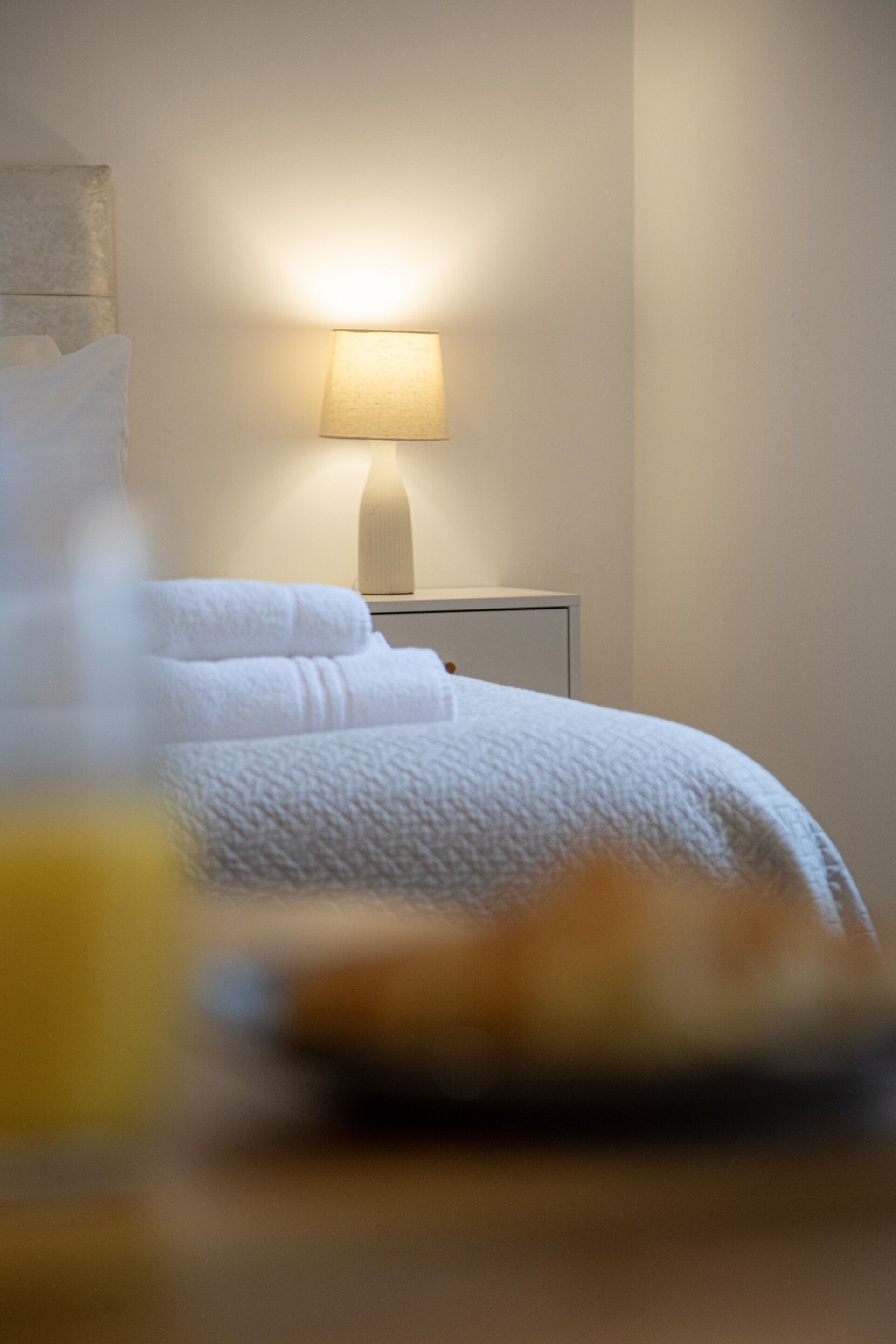 Ein ordentlich bezogenes Bett mit weißen Leinen und einer Nachttischlampe.