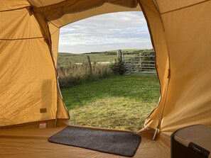 A tent with a view of a grassy field and a metal gate.