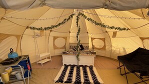 A tent with a bed, a small table, a chair, and a shelf with items. - Impeccable 1-bed Bell Tent Near Holyhead (Holyhead)