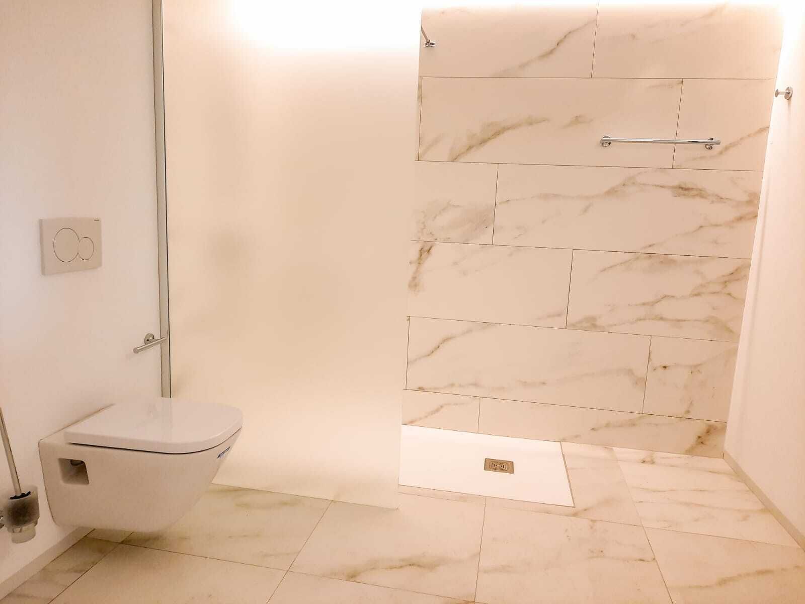 Une salle de bain comprenant des toilettes, une douche aux carreaux de marbre et un sol au motif similaire.