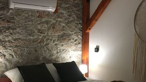 A bed with a wooden headboard, a stone wall, and a white air conditioning unit above it. - Apartment Equinox-Island Pag (Pag)