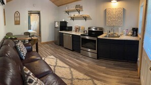 A compact living space with a brown leather sofa, a dining table, a kitchen area with a refrigerator, microwave, stove, and sink. - Cana Cottage | Farm Stay (Tyler)