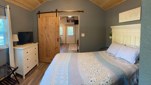 A bedroom with a bed, a dresser, a TV, and a sliding door leading to another room. - Cana Cottage | Farm Stay (Tyler)