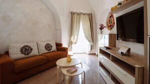 A living room with a brown sofa, a small round table, a flat-screen TV, and a wooden TV stand.