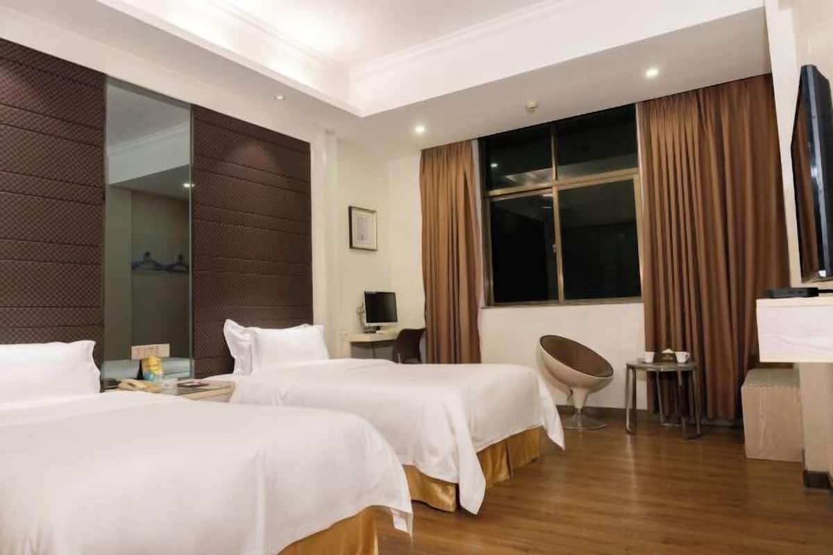 Une chambre d’hôtel avec deux lits, un bureau, une chaise, une télévision et une fenêtre avec des rideaux.