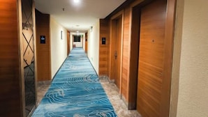 Ein Hotelkorridor mit blauem Musterteppich, Holztüren und modernem Design.