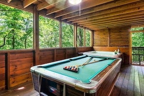 Enjoy a game of pool in a cozy cabin with a high ceiling and large windows offering a view of the surrounding forest.