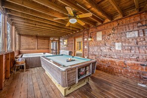 Relax in this rustic room with a pool table and seating area, featuring a ceiling fan and windows for a view.
