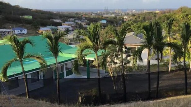 A view of a residential area with houses, a green-roofed building, and palm trees. - 3 BR/ 2 full baths unit with south shore view. (Christiansted)
