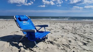 Uma praia com uma única cadeira de praia azul com a marca 'Tommy Bahama' na areia.