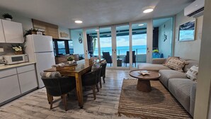 A modern kitchen with a dining area, a living room with a sofa, and a view of the ocean through large glass doors. - Guest Favorite • Beachfront Luquillo Condo • Walk to Kioskos & El Yunque (Luquillo)
