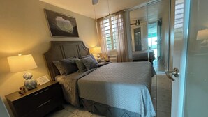 A bedroom with a bed, nightstands, a lamp, and a painting on the wall. - Guest Favorite • Beachfront Luquillo Condo • Walk to Kioskos & El Yunque (Luquillo)