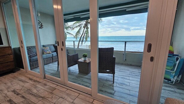 A balcony with wicker furniture, a small table with a plant, and a view of the ocean. - Guest Favorite • Beachfront Luquillo Condo • Walk to Kioskos & El Yunque (Luquillo)