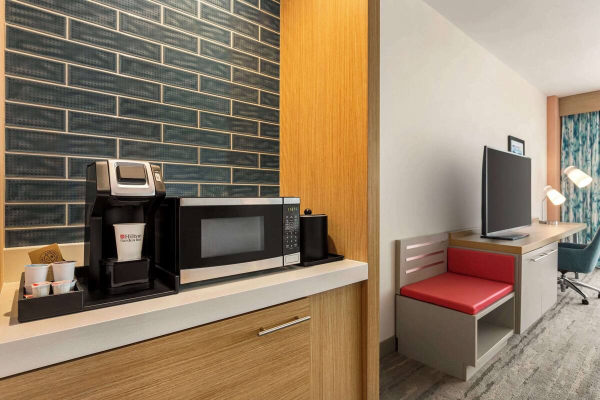 Ein kompaktes Hotelzimmer mit Küchenzeile, Fernseher, Schreibtisch mit Stuhl und einer kleinen Sitzecke.