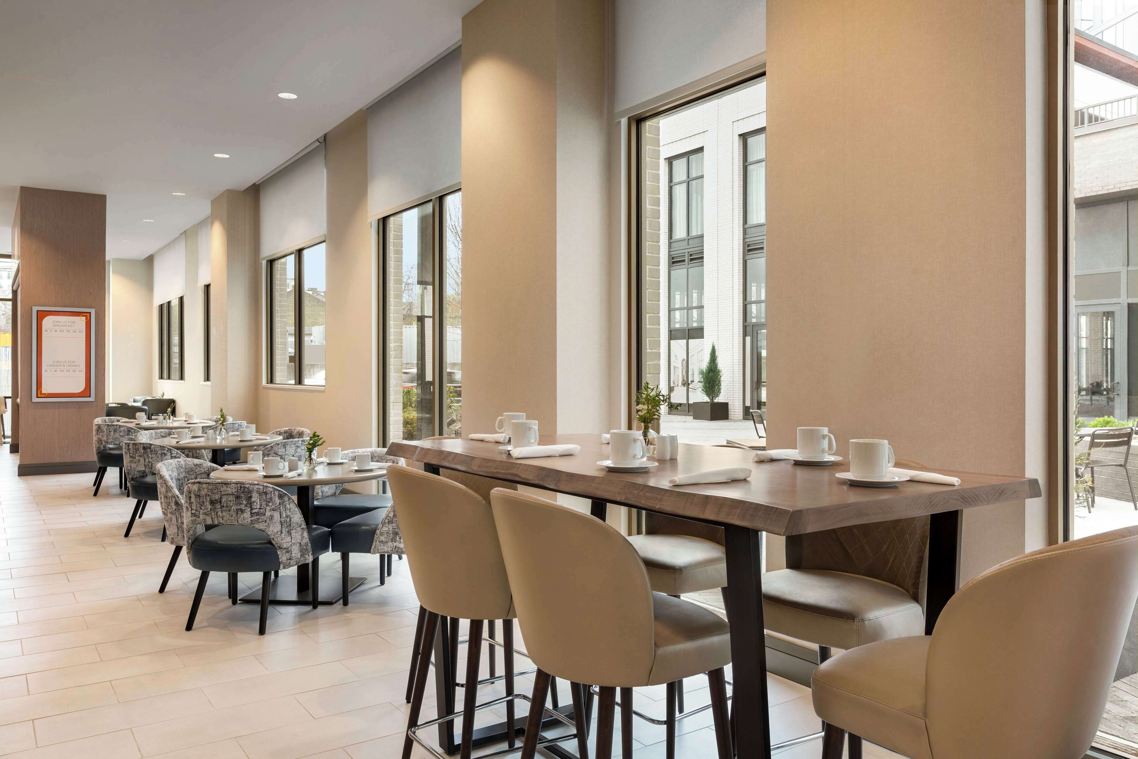 Un espace de restauration moderne, doté de longues tables et de chaises, de grandes fenêtres et d’un aménagement épuré et minimaliste.