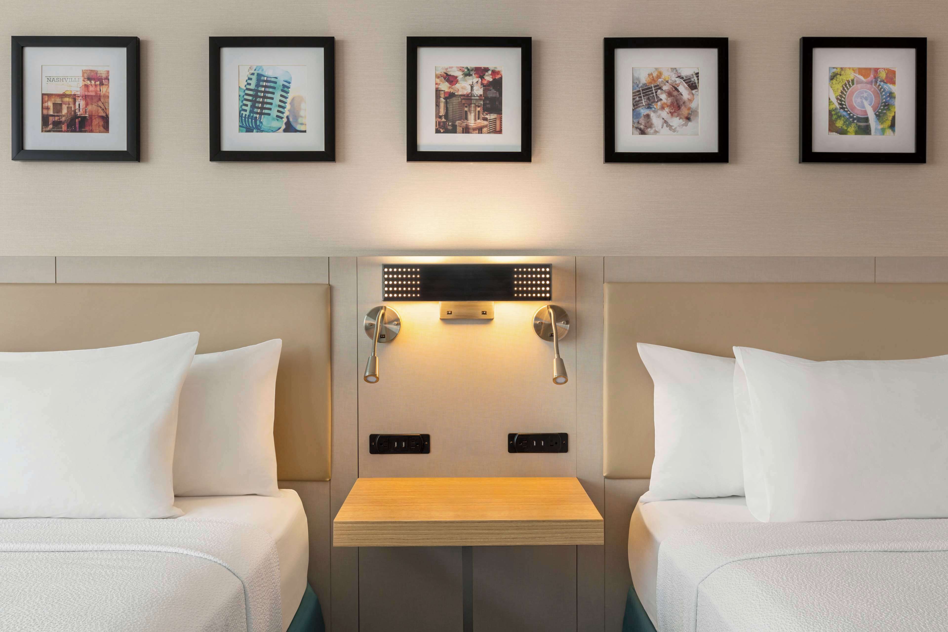 A hotel room with two beds, a small table, and a wall-mounted light fixture.