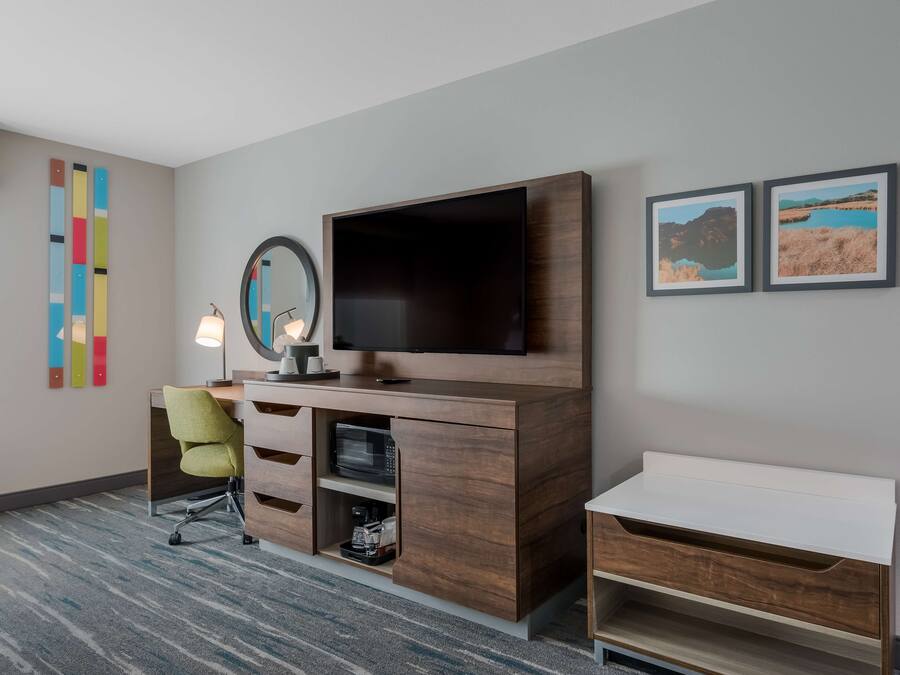 Een hotelkamer met een houten bureau, een televisie, een lamp en twee ingelijste foto’s aan de muur.