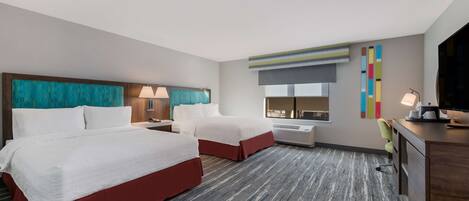A hotel room with two beds, a desk, a chair, a TV, and a window with a view.