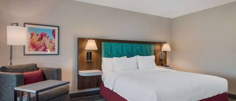 A hotel room with a large bed, a sofa, a small table, and two bedside lamps.