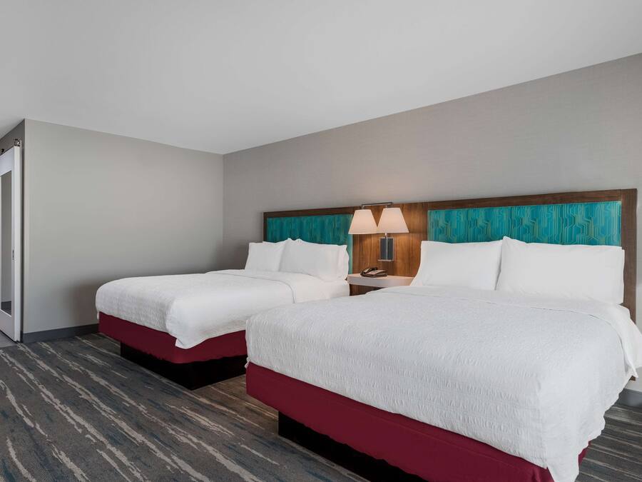 A hotel room with two beds, a wooden headboard, a nightstand with a lamp, and a door leading to another room.