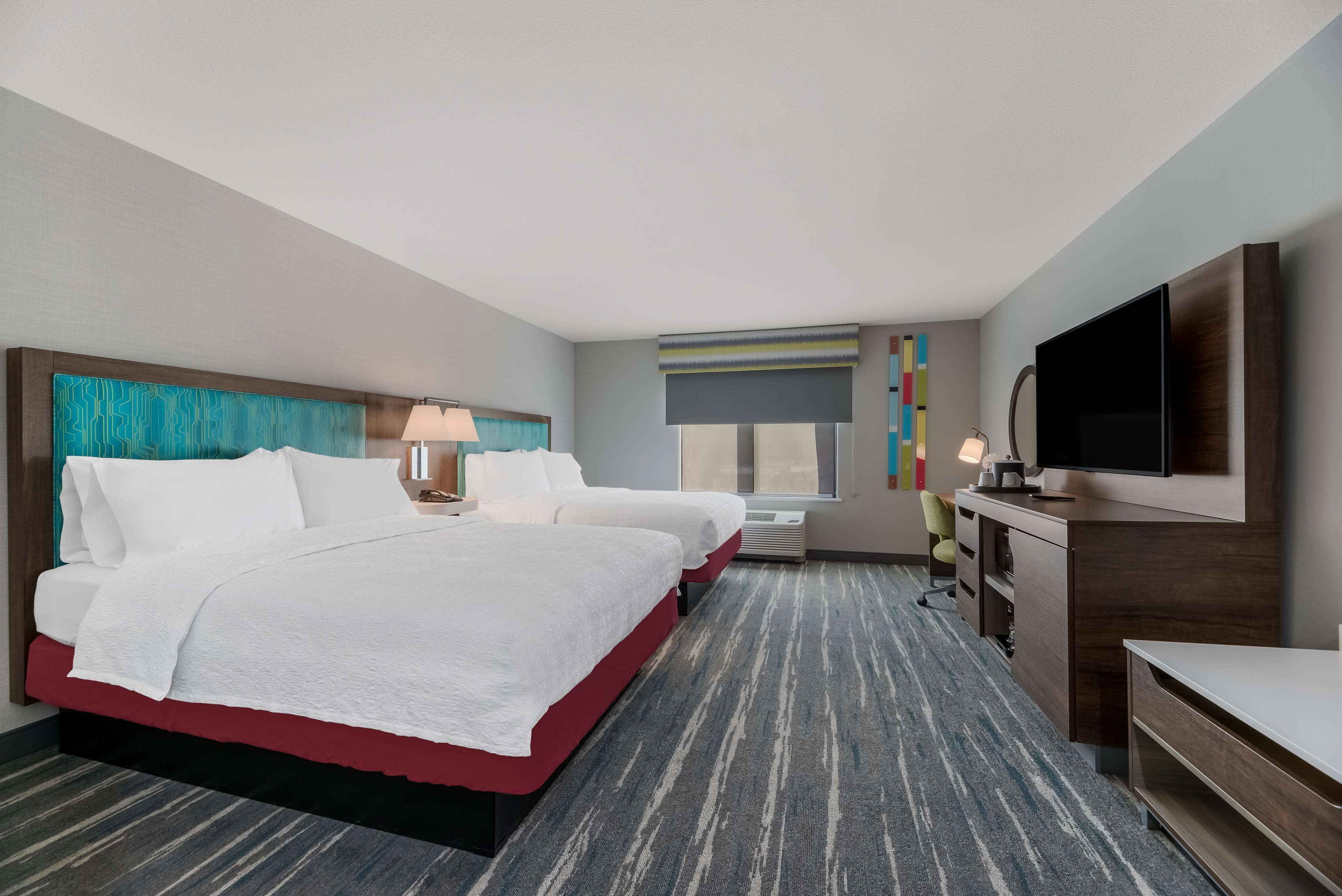 A hotel room with a large bed, a desk, a TV, and a window with a view.