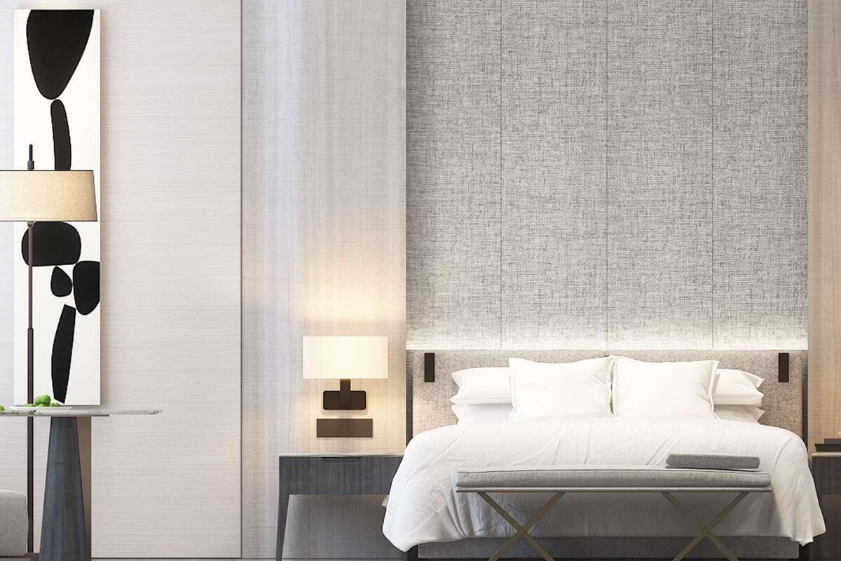 Una habitación de hotel moderna con cama, mesitas de noche, un espejo grande y un baño con tocador y lavabo.