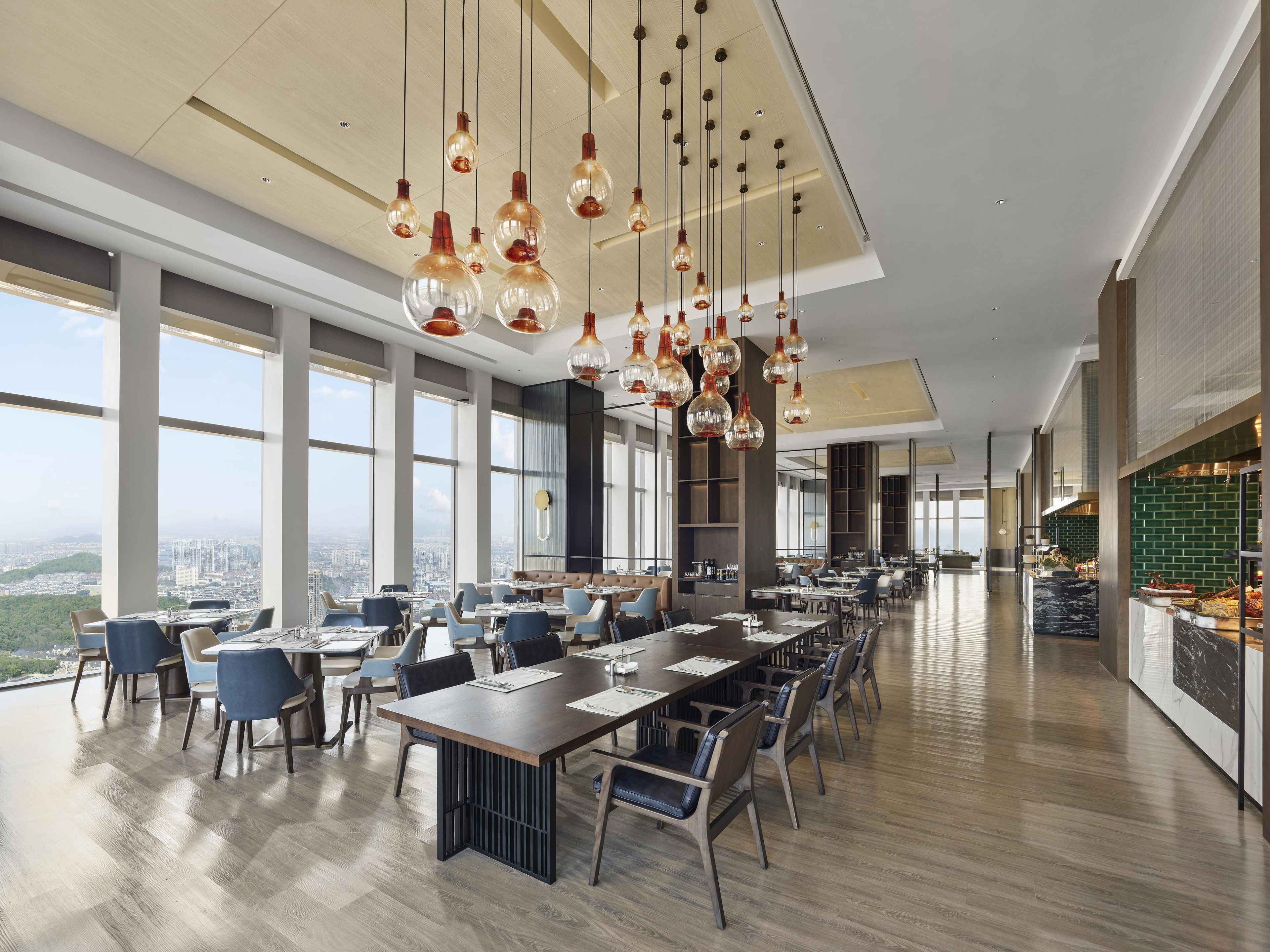 A modern dining area with high ceilings, large windows, and hanging pendant lights.