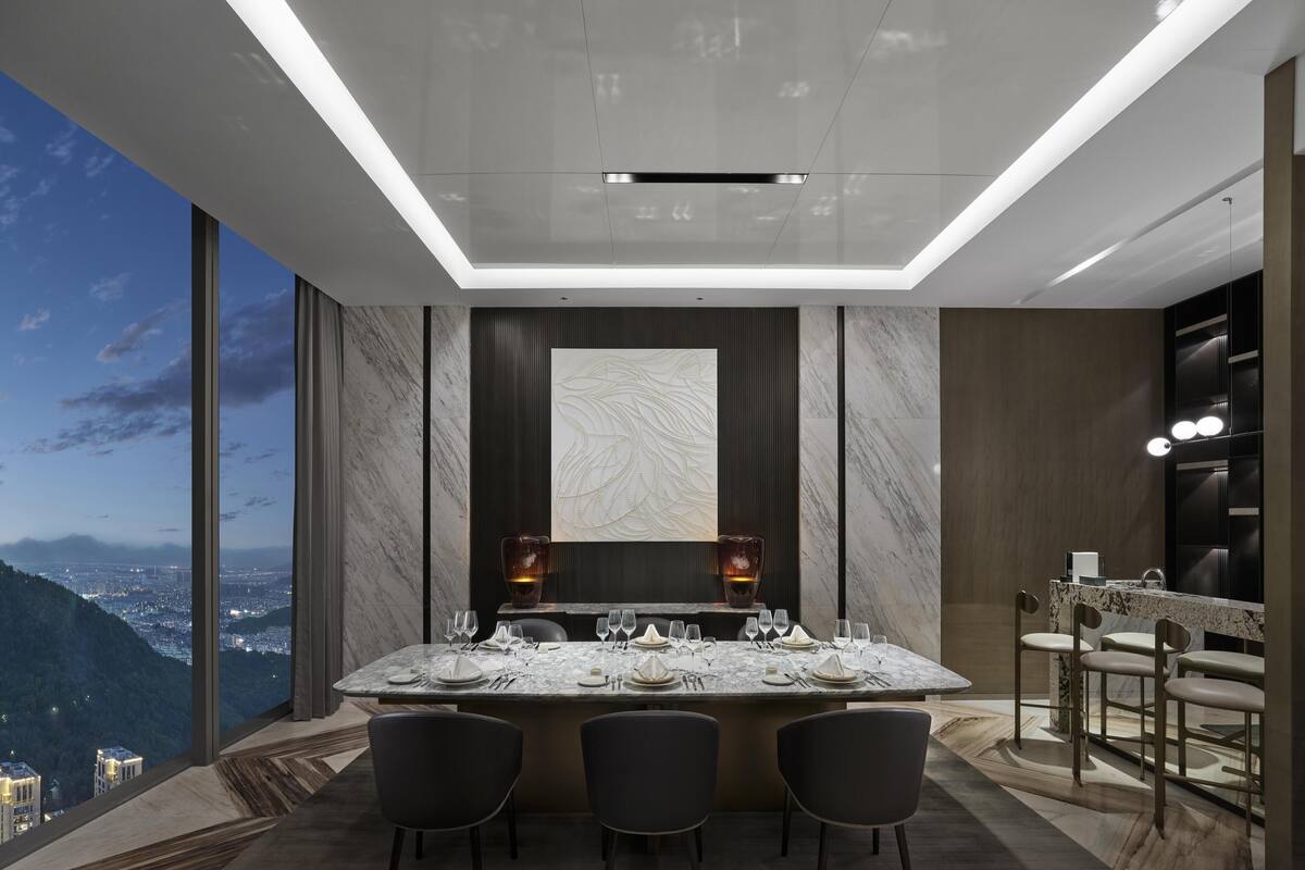 A modern dining area with a large marble table, dark chairs, and a city view.