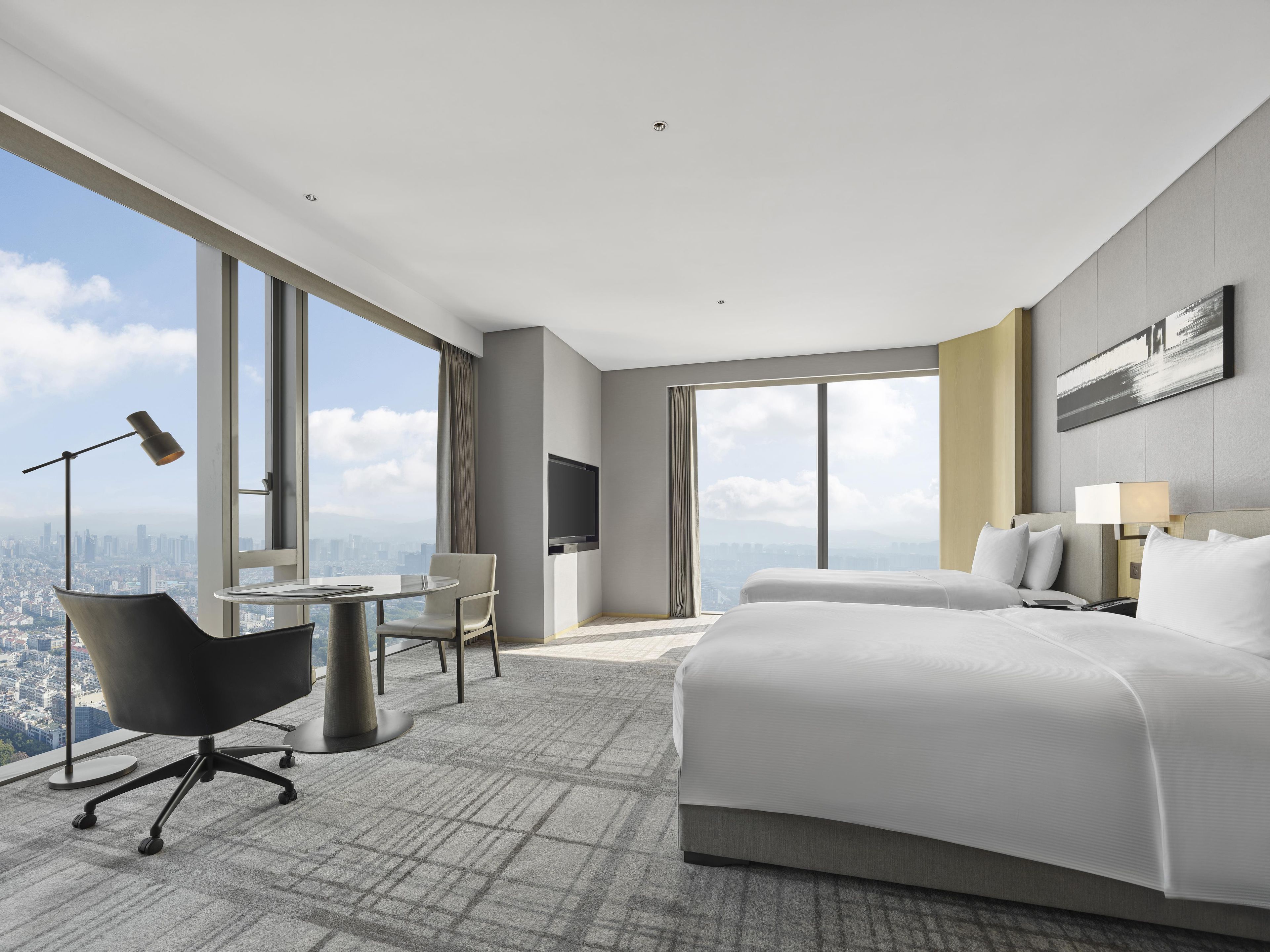 Una habitación de hotel moderna con una cama grande, un escritorio, una silla, un televisor y vistas a la ciudad.