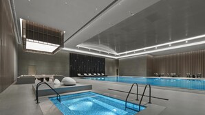 A modern indoor swimming pool with a rectangular shape, surrounded by lounge chairs and a seating area with a poolside bar. - Hilton Zhuji (Shaoxing)