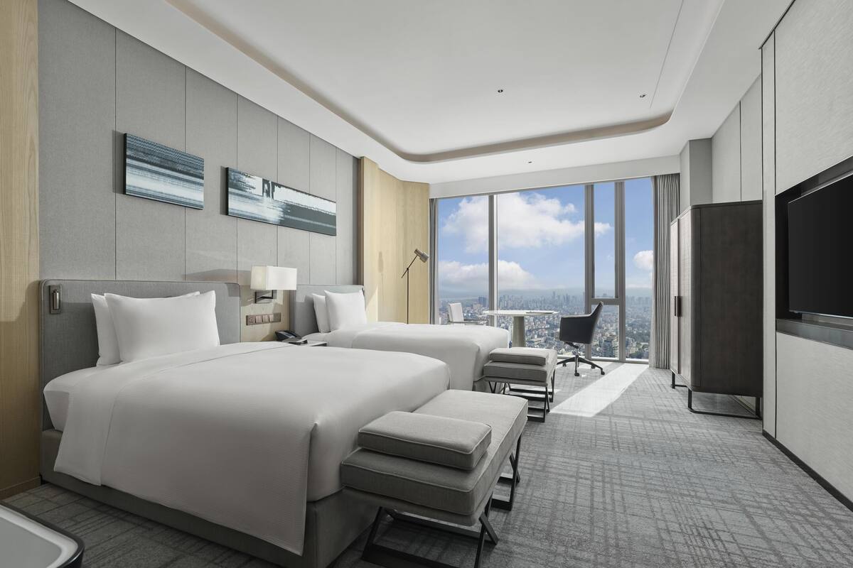 A modern hotel room with a large bed, two bedside tables, a desk, and a chair.