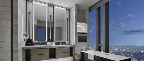Un baño moderno con un espejo grande, lavamanos dobles, una bañera y vistas a la ciudad.