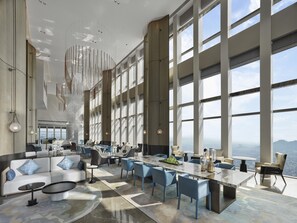 A spacious hotel lobby with a large seating area, a central bar, and large windows offering a city view. - Hilton Zhuji (Shaoxing)