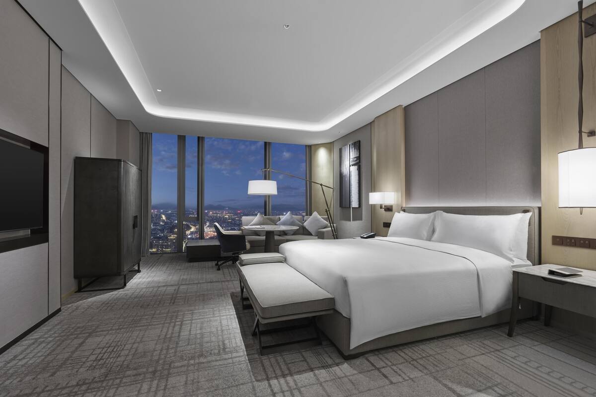 A modern hotel room with a large bed, bedside tables, a desk, and a view of the cityscape.